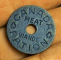 Obverse of blue Canadian meat ration token held in fingers