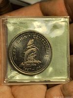 Obverse view of coin in plastic showing fish design and centennial dates