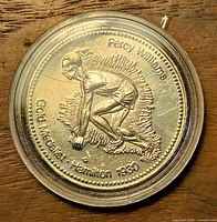 Obverse view of coin in capsule showing Percy Williams and inscriptions