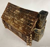 Angled view of glazed ceramic log cabin cookie jar showing roof, walls, chimney