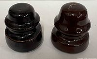 Front view of two dark brown porcelain insulators