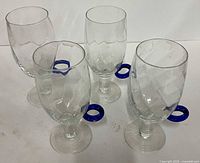 Four clear glass pedestal coffee cups with blue handles grouped together