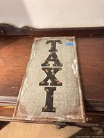 Front of galvanized metal sign showing "TAXI" lettering and rust wear