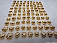 Grid layout of 100 identical gold-plated Om signet rings