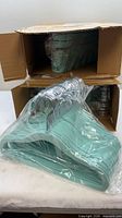 Two cardboard boxes each containing a plastic-wrapped bundle of mint green velvet kids hangers