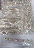 Multiple sealed bags of faux pearl necklaces grouped by dozen
