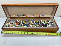 Wooden box open showing full quantity of marbles with tape measure for scale