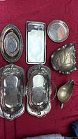 Group shot of all seven silver-toned serving pieces on red background