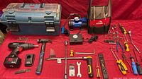 Overall lot layout on red cloth showing toolbox, tote, air compressor, drill, hammer, hand tools