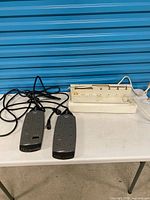Overview of two gray surge protectors and one white wall-mount surge station on table