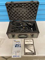 Document camera with cables in open hard case, manuals beside case