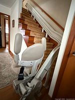Full view of stairlift chair mounted at base of staircase on rail
