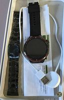 Smartwatch in box with spare strap, charger and manual visible