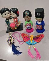 Group view of ceramic family figurine, two wooden dolls, woven shoes pair and butterfly ornament