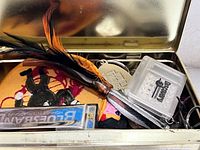 Open Camel tin showing harmonica, Discovery Channel case, feather, patch and assorted small items