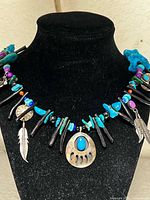 Close-up of necklace on display bust highlighting bear paw pendant, turquoise nuggets, black beads, and feather charms
