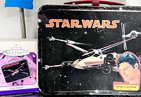 Front view of lunchbox with STAR WARS logo, X-Wing art, Superman sticker and boxed Hallmark ornament