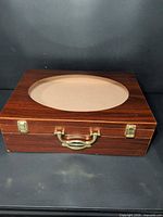 Closed box top view showing wood veneer, oval glass window, brass handle and latches