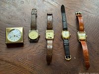 Group shot of four wristwatches and brass Swiza desk clock