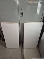 Two white MDF shelf boards leaning against metal cabinet