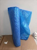 Rolled blue bubble-sheet solar pool cover leaning against wall