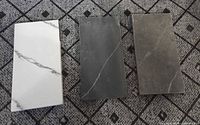 Three quartz slabs on patterned background: white, charcoal, taupe-grey