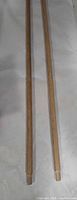 Pair of wooden broom handles laid side by side showing full length and threaded tips