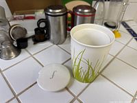 Overview of countertop with paper cup foreground, stainless mugs and accessories in background