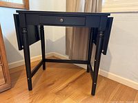 Front view of black drop-leaf table desk with both leaves down showing drawer and legs