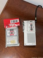 Front view of Sanyo TMC-1000 recorder with wrist strap beside sealed Sony MC60 tapes