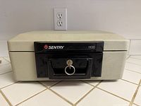 Closed Sentry 1100 safe front view showing lock, handle, key inserted