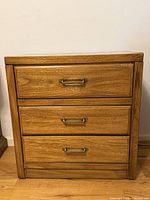 front view of wooden nightstand showing three drawers and metal pulls