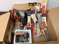 Box view: drill with orange cord and packaged bits