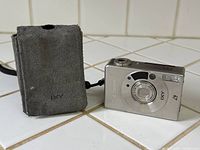 Front view of Canon IXY 320 camera next to suede pouch