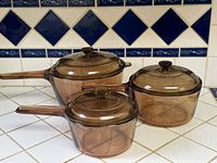 Three amber glass Corning Visions saucepans with lids grouped together