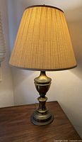 Full view of brass urn table lamp with shade on wooden surface