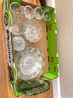 Box containing multiple clear glass pieces including dessert bowls, small dishes, lidded compote and large platter