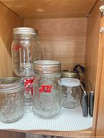 Assorted Ball jars with lids and jar lifter inside cabinet