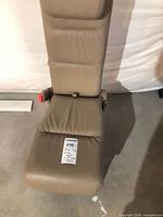 Front view of beige jumpseat showing headrest, seat cushion and attached seatbelt buckle