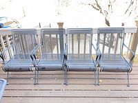 Four black metal mesh patio chairs on deck