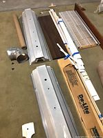 Overall view of troffer housings, shelving panels, wood boards, duct elbow, rolls