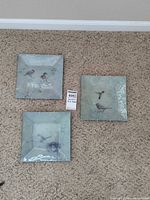 Three square bird plates on carpet