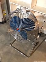 Front view of Lakewood chrome fan with blue blades on wheeled stand