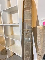 Rug rolled and tied with twine leaning against shelving