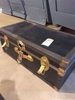 Full view of closed black trunk showing top, side and brass latches