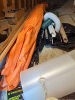 Orange tarp, vent duct, garden hose, lumber planks, corrugated plastic sheet, assorted pipes, cardboard box