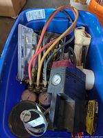 Overview of lot in blue tote showing manifold gauges, colored hoses, vacuum pump, accessories