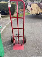 Front view red steel hand truck showing frame, toe plate, wheels; small chrome cart nested