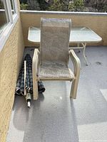 beige sling chair, glass patio table, folded striped umbrella on balcony
