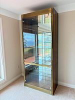Front view of tall wood veneer curio display cabinet showing glass doors, brass trim, and interior shelves